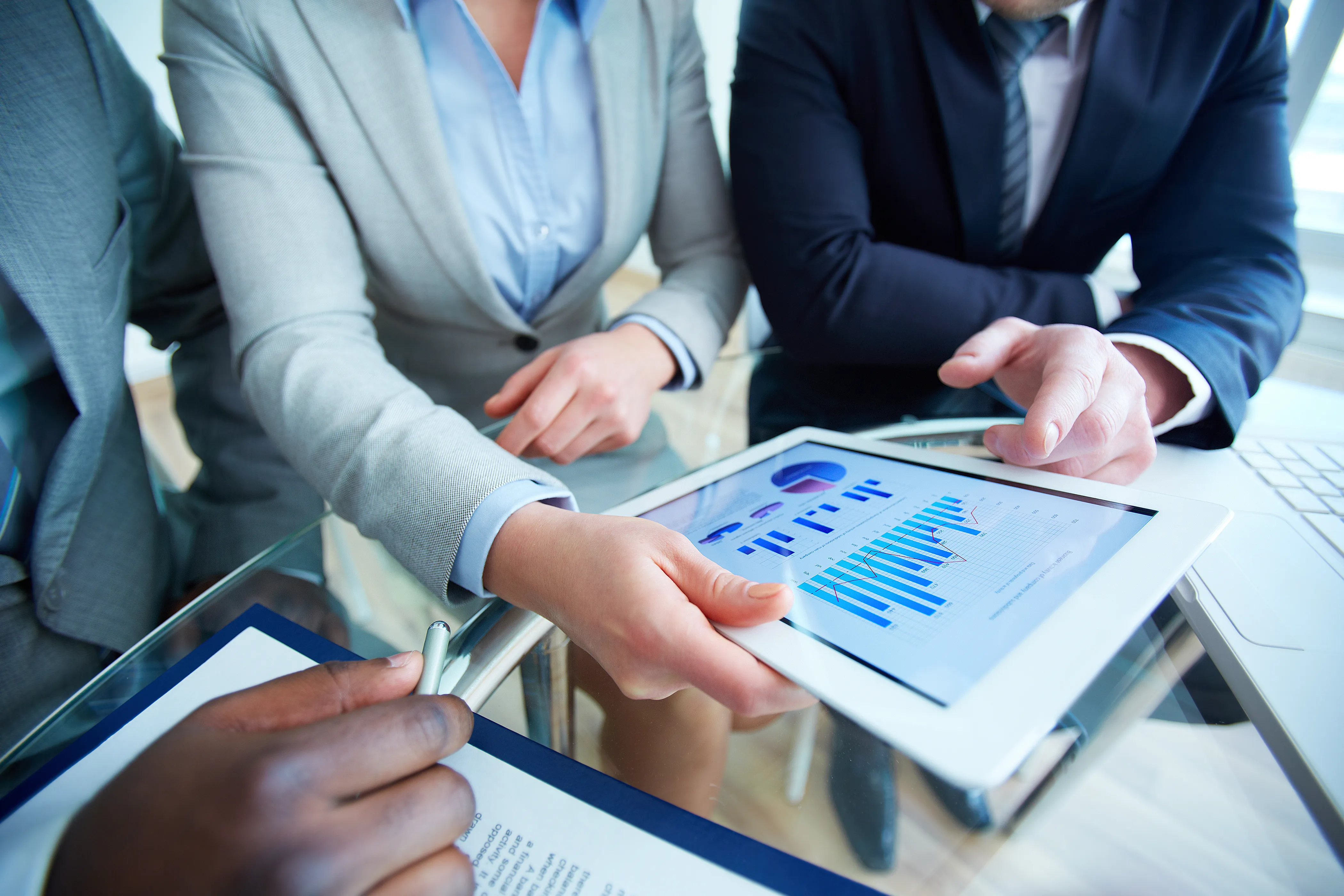 Businesspeople shaking hands in an office with colleagues watching and smiling.