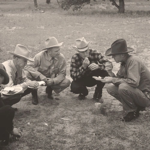Vintage image of a group of cowboys kneeling together in a pasture.