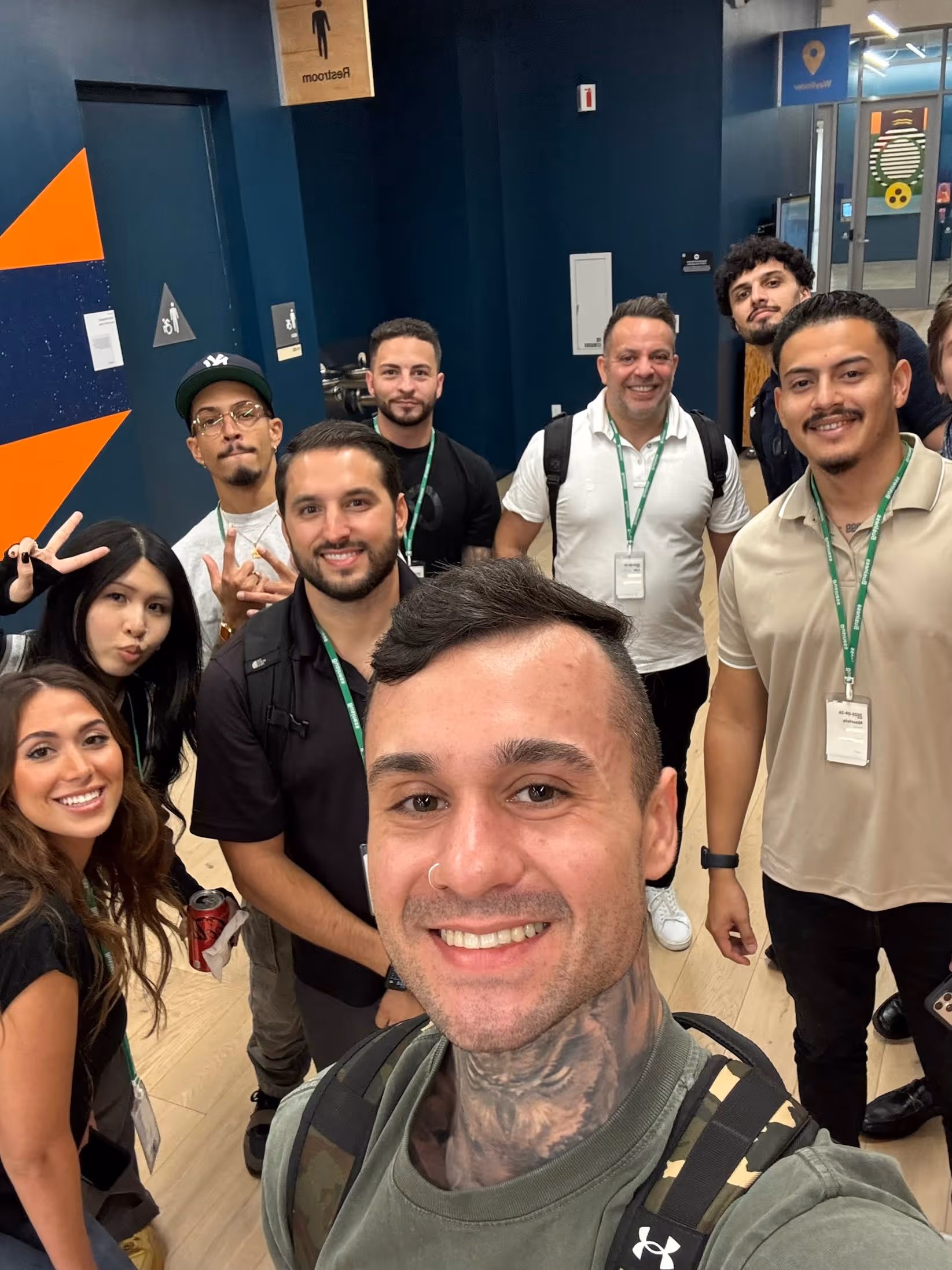 Smiling group selfie of nine diverse young adults in a brightly lit indoor space.