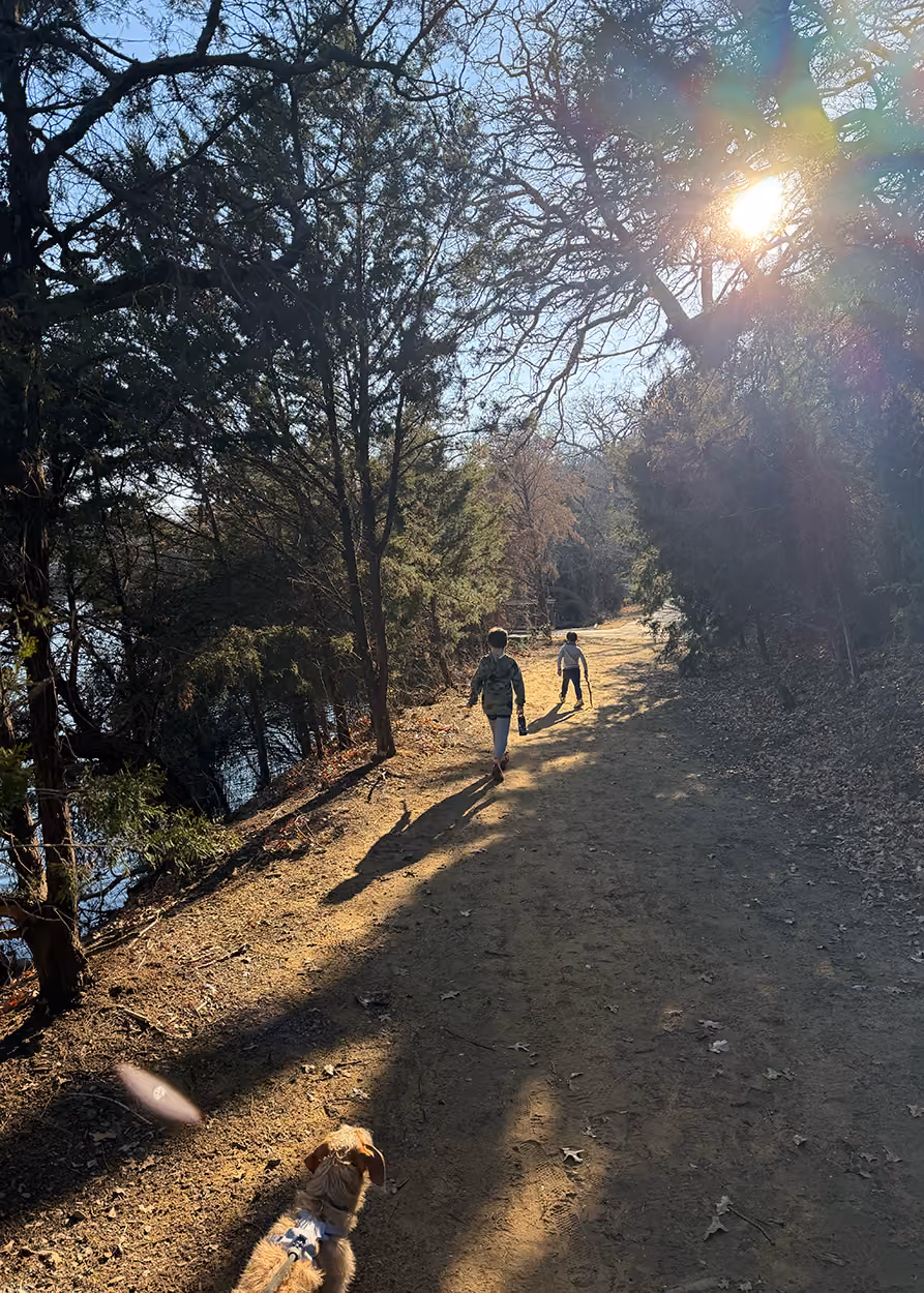 Two children walking on a dirt path through a wooded area with a dog following behind them. James Bass, owner of James Bass Counseling in Plano TX