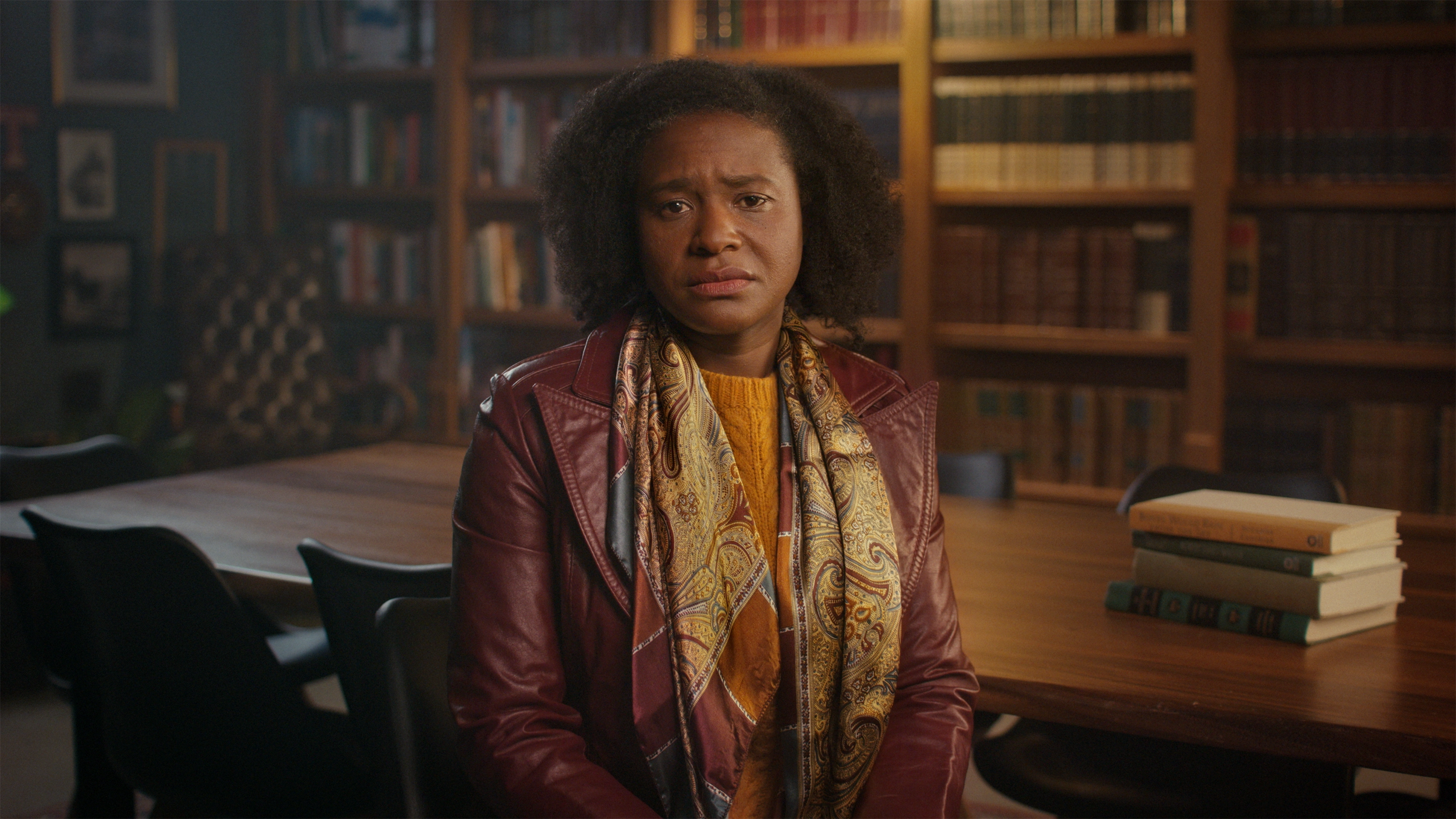 A Black middle-aged person seated in a library.