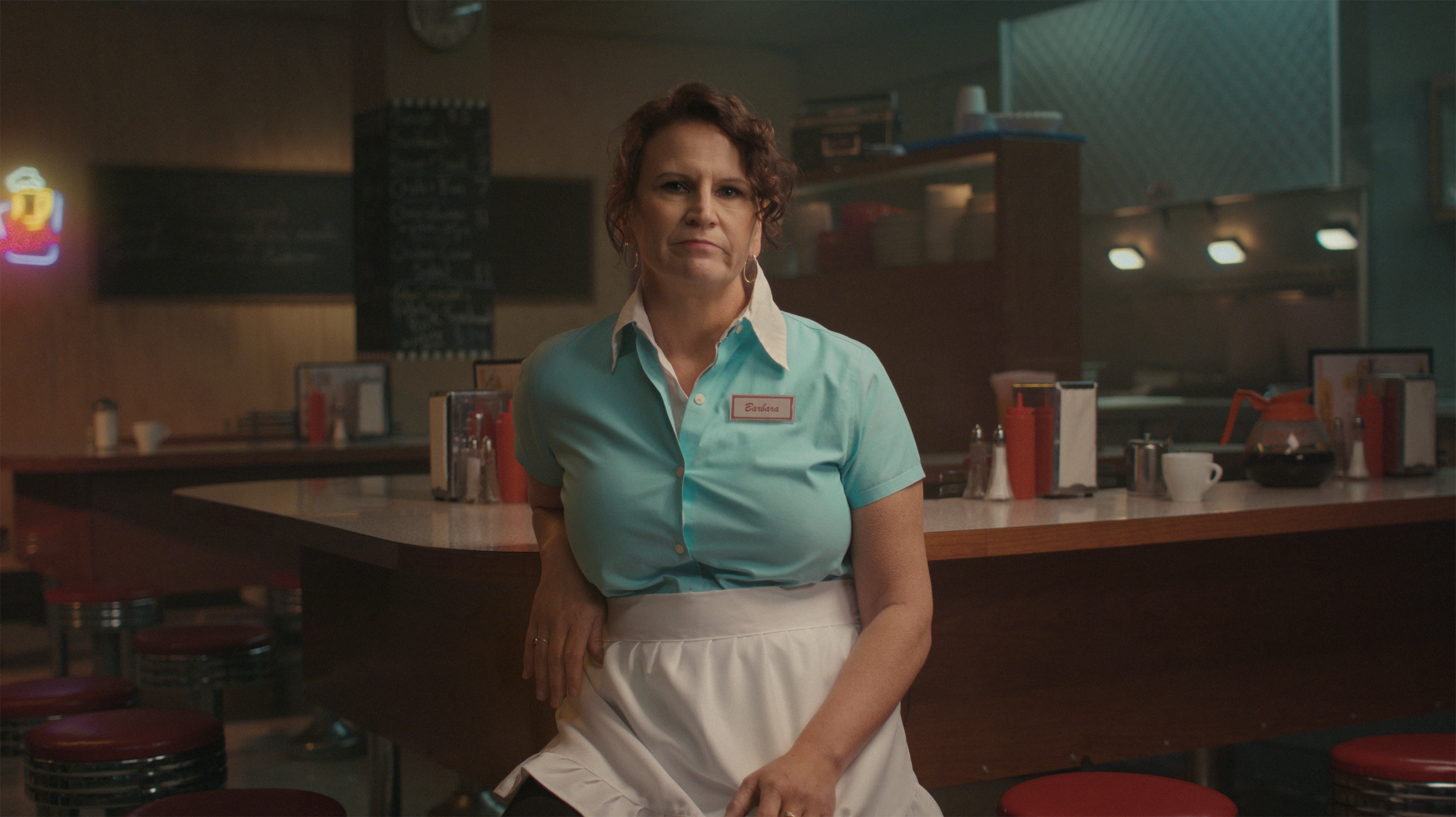 A middle-aged person dressed in a server's uniform at a restaurant.