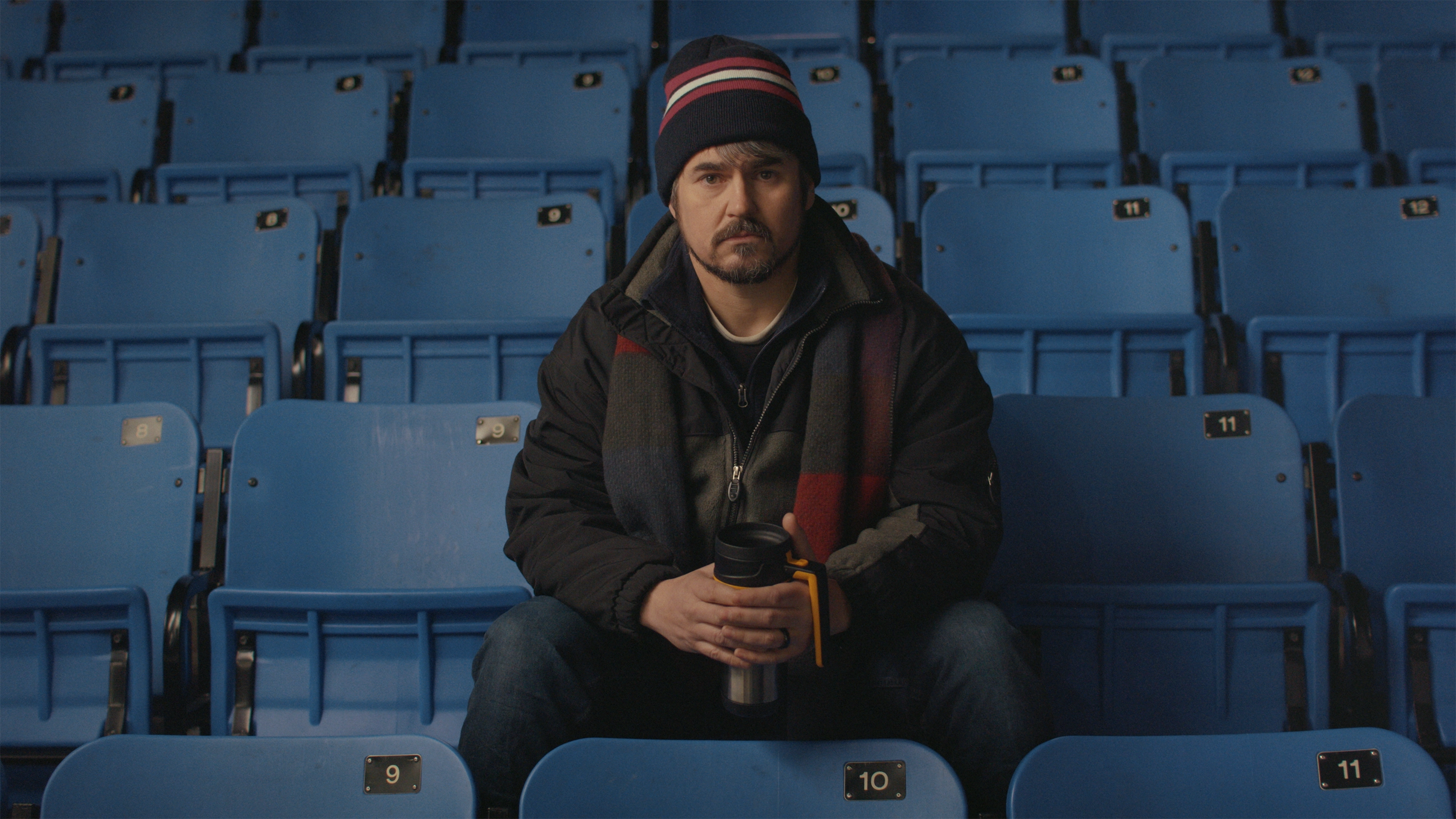 A middle-aged white person seated in a hockey arena.