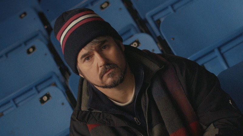 A white, middle-aged man seated in a hockey arena.