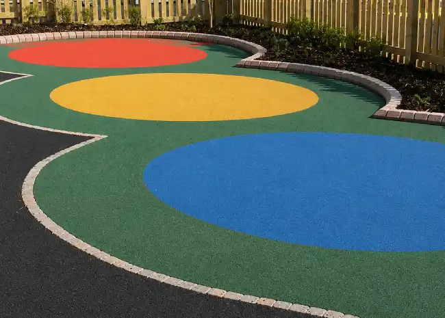 Colorful playground surface with green, blue, yellow, and red circles on mbresinbound rubber bound flooring.