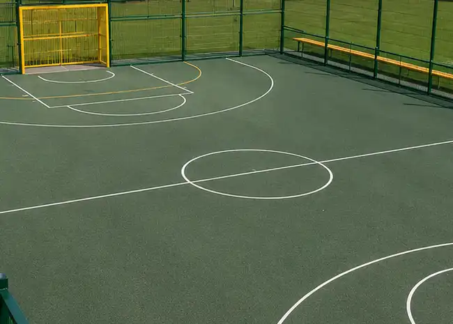 Resin bound commercial projects Outdoor sports court with basketball markings, a yellow goal, and wooden benches along the fence.