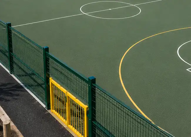 Outdoor sports court with green fencing and a yellow gate beside the white and yellow court lines. 