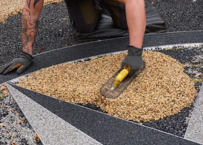 Person with gloves using a trowel to spread resin bound granules in a decorative compass design.