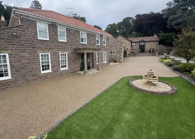 Stone house with white windows, tiled roof, green lawn, and a small stone fountain in front.