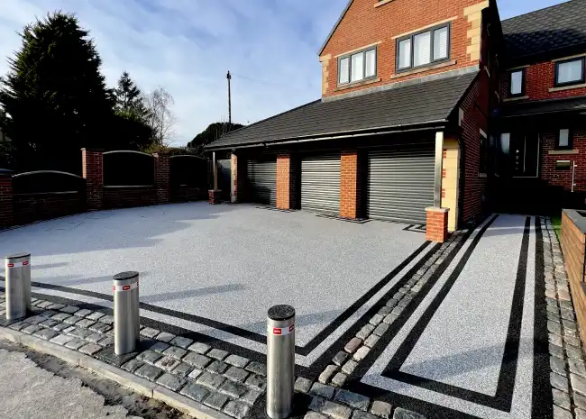 Driveway with bollards and three closed garage doors on a brick house under a blue sky.