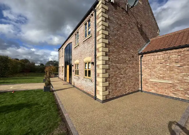 Two-story brick house with large windows, gravel driveway, green lawn, and cloudy sky.