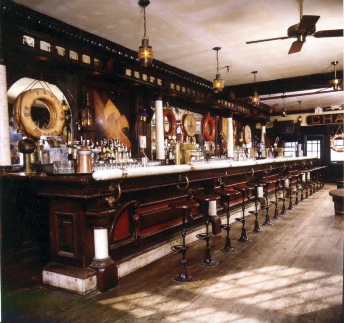 Bar stools at a high-top table inside The Captain Kidd, with a carved wooden fish and an American flag overhead