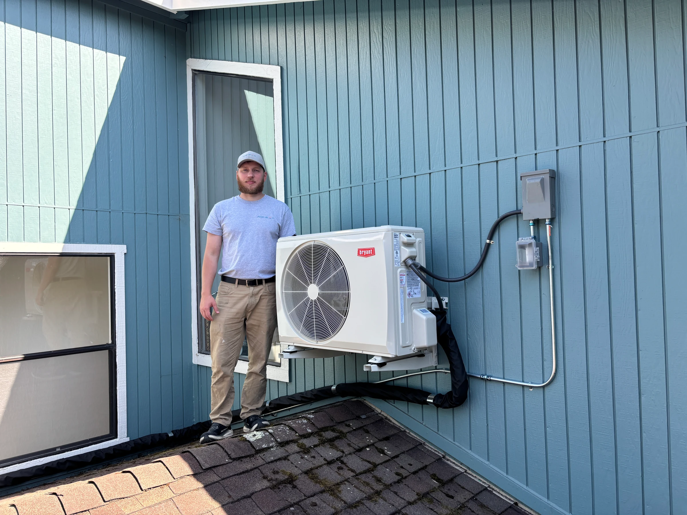 Plug-In Services technician beside a wall-mounted Bryant heat pump