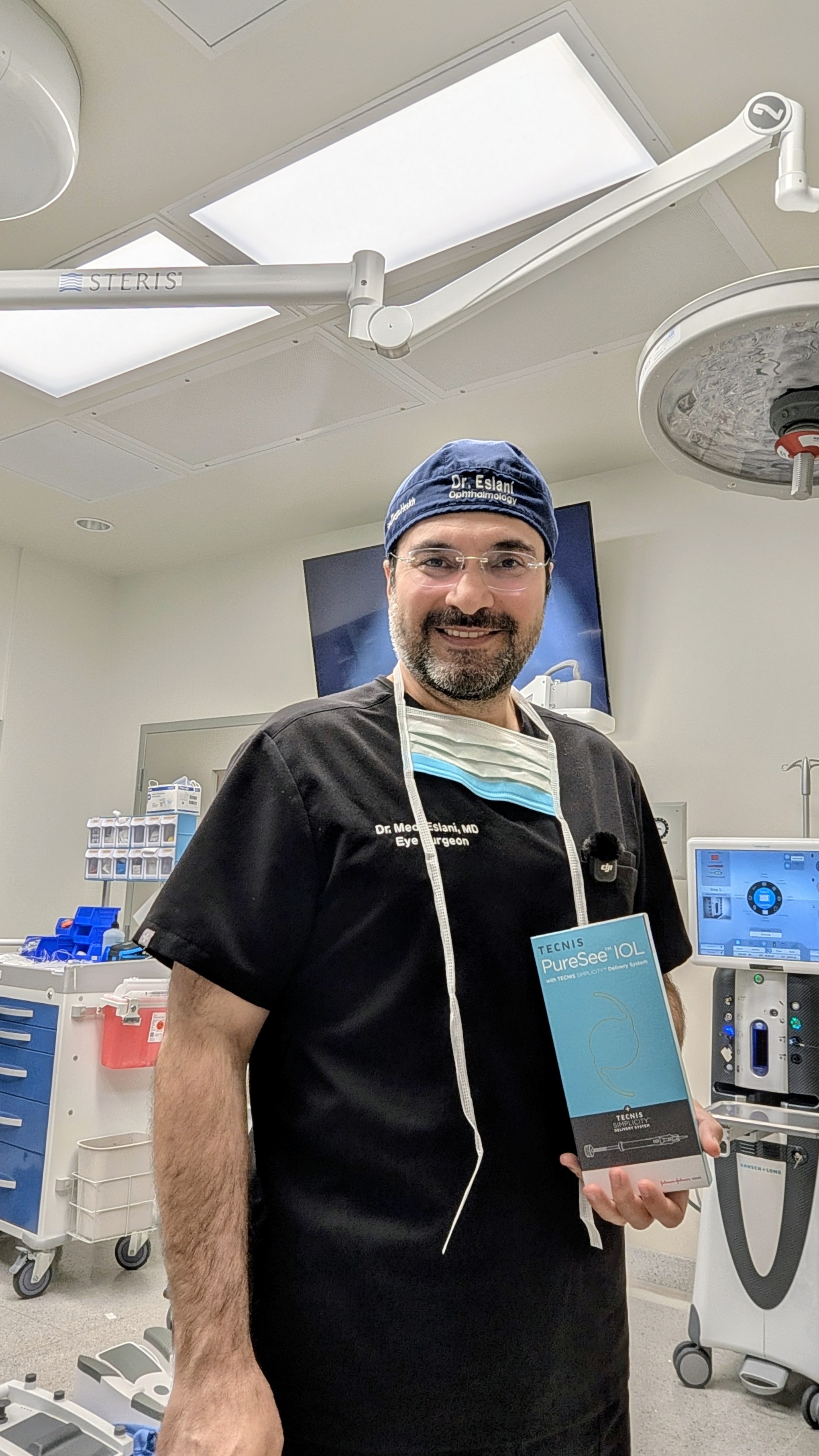 Medi Eslani, MD, FAAO in the operating room holding a TECNIS PureSee intraocular lens