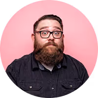 Man with glasses and a full beard wearing a dark shirt against a pink background.