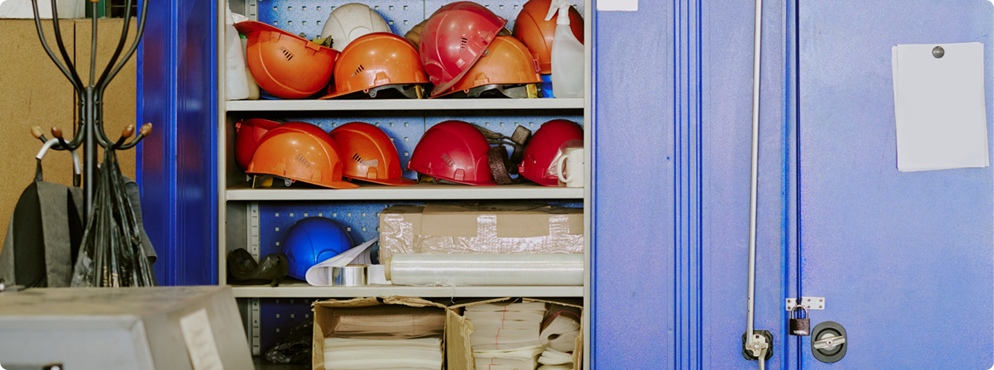 Pack N Stor self-storage business Shelves with orange, red, and blue hard hats and boxes beside a locked blue metal cabinet.
