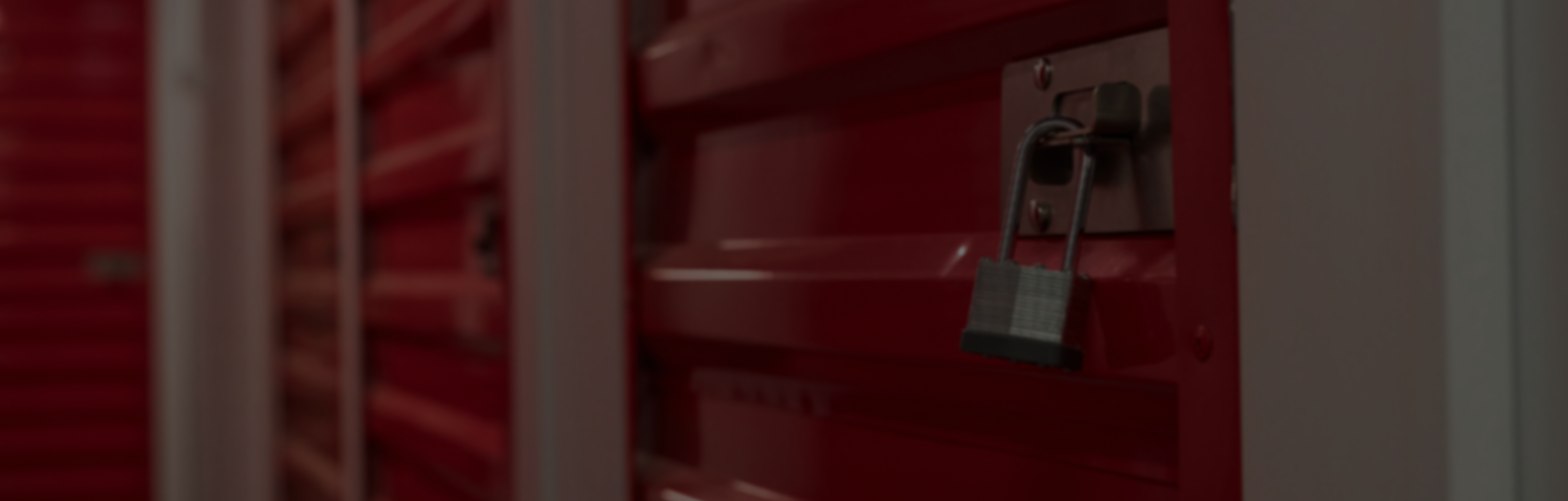 Pack N Stor self-storage Close-up of a silver padlock securing a red metal storage unit door in a row of similar units.