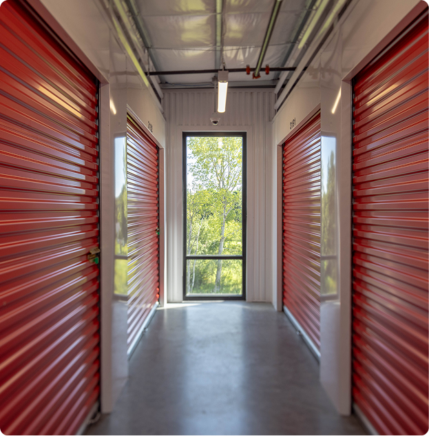 Pack N Stor self-storage Hallway with red roll-up doors on both sides in an indoor storage facility with a window at the end.