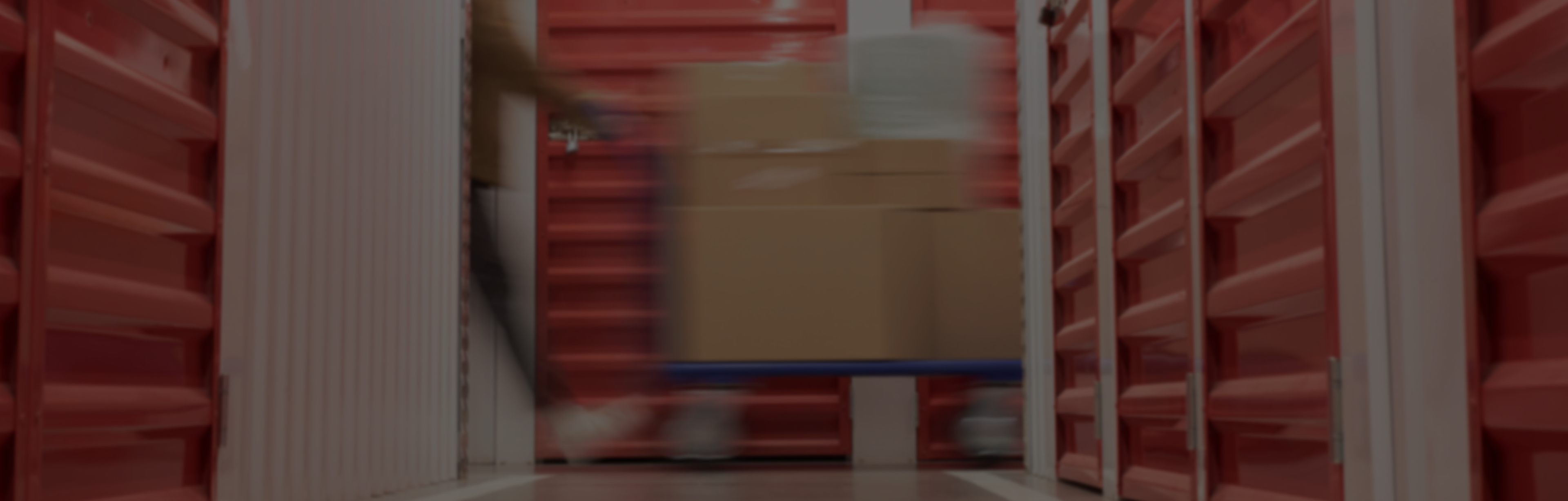 Pack N Stor self-storage Blurred person moving a blue cart stacked with cardboard boxes in a storage facility hallway.