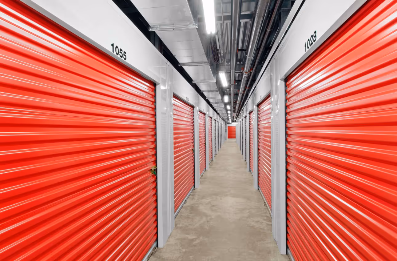 Pack N Stor East Fishkill NY, Indoor storage facility corridor with rows of closed red metal roll-up doors on both sides.