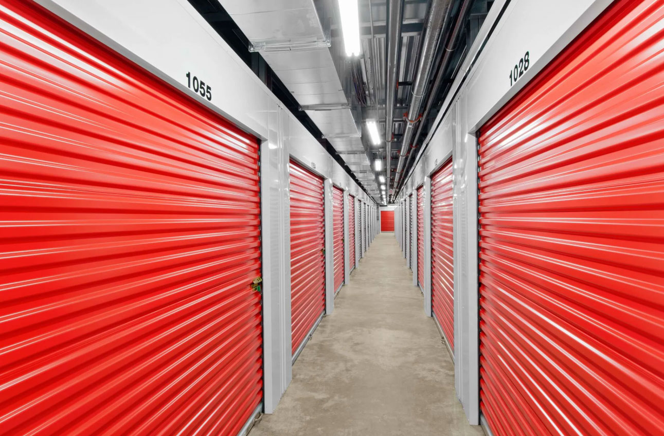 Pack N Stor East Fishkill NY, Indoor storage facility corridor with rows of closed red metal roll-up doors on both sides.