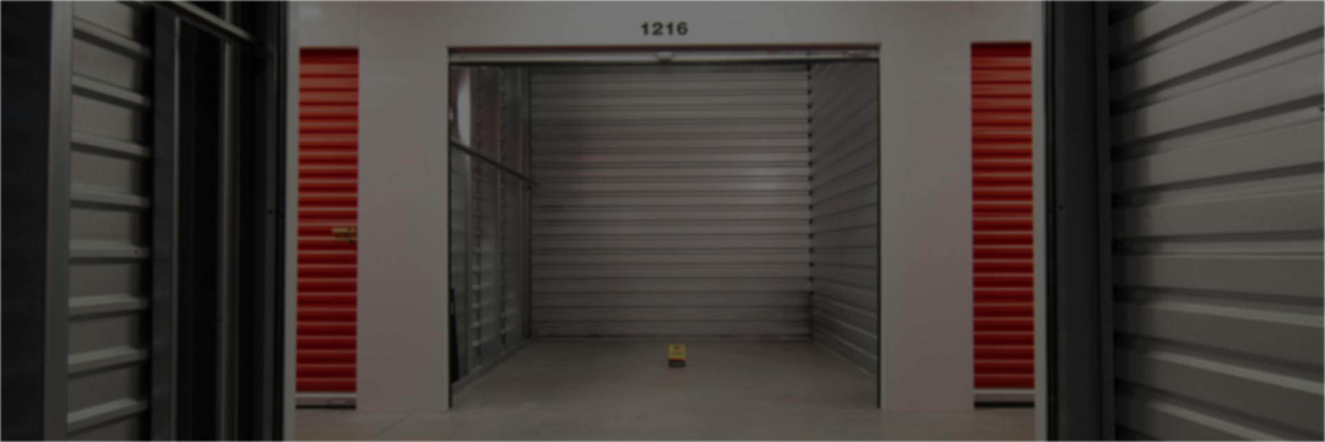 Pack N Stor Self-Storage Empty storage unit with gray roll-up door and red side panels in a clean warehouse.