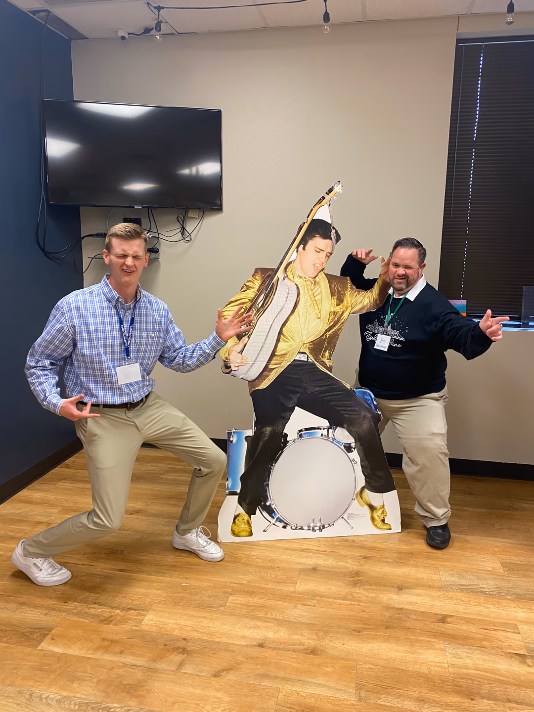 Two men posing energetically on either side of a cardboard Elvis Presley cutout playing guitar.