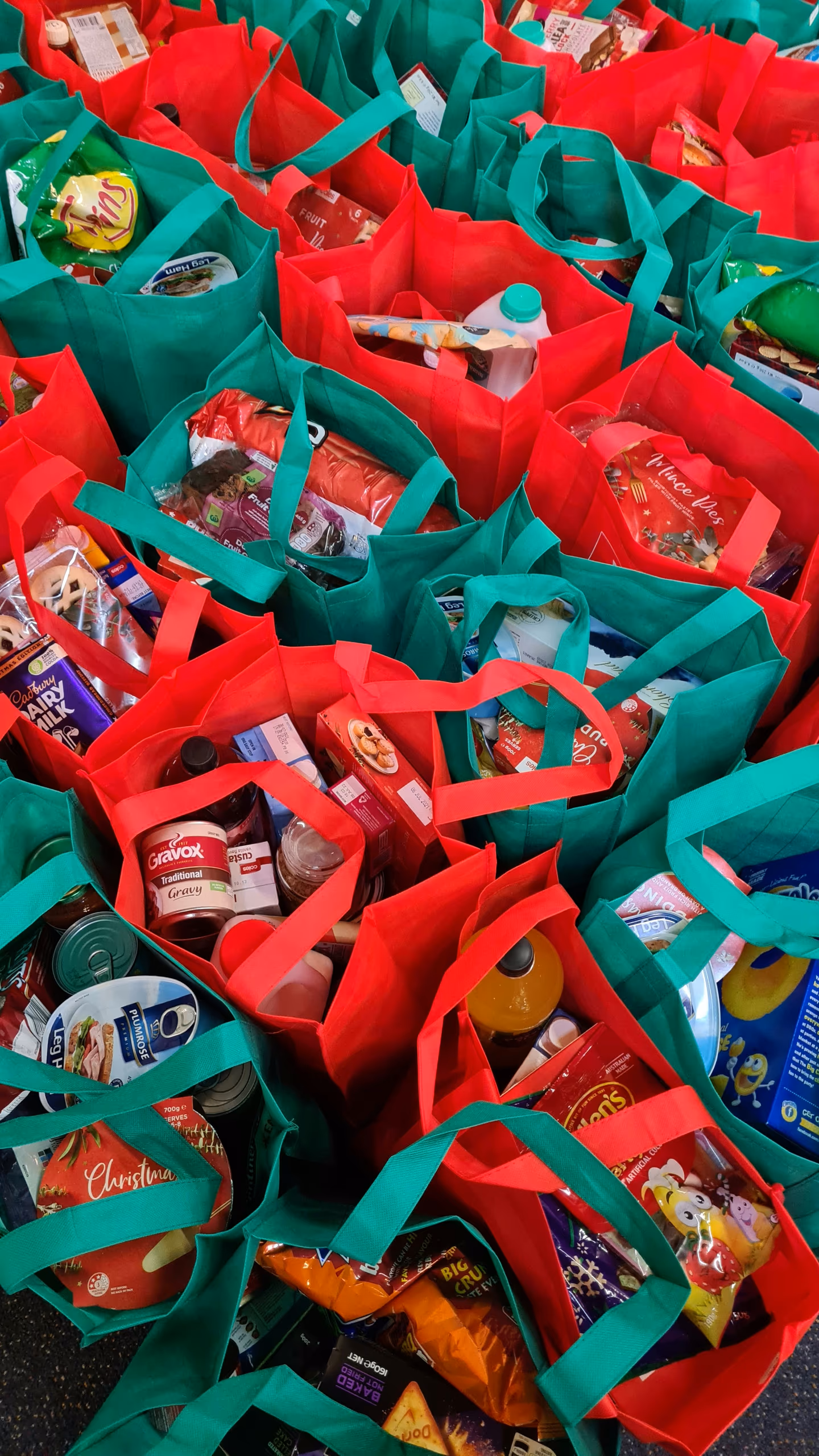 Multiple red and green reusable bags filled with assorted groceries and food items.