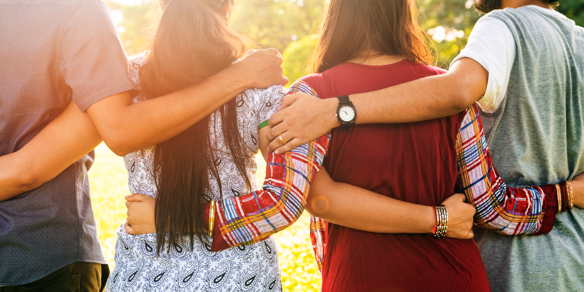 Group of people standing close outdoors with arms around each other’s backs showing friendship.