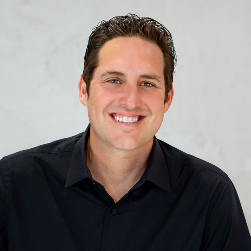 Smiling man with short dark hair wearing a black collared shirt on a light background.