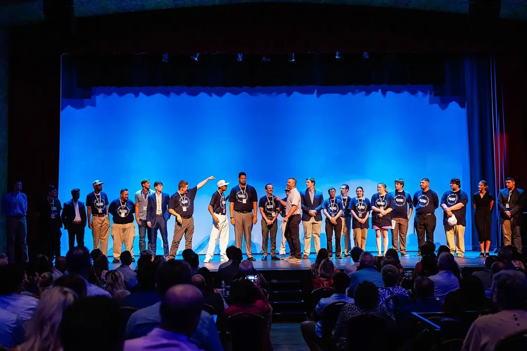 Group of people standing on stage in front of an audience under blue lighting.