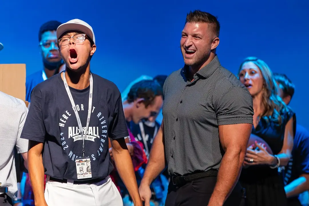 Two men laughing and reacting excitedly on stage with a blue background and people behind them.