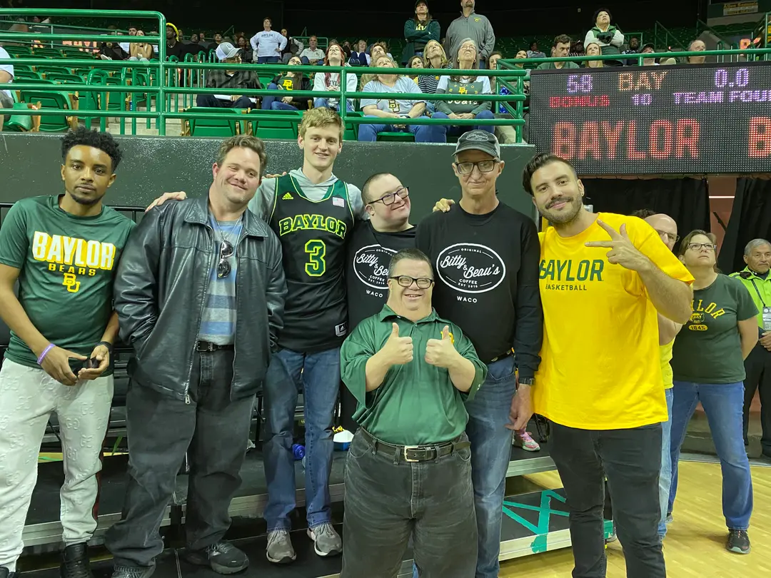 Group of men posing together at a Baylor basketball game with scoreboard in background.