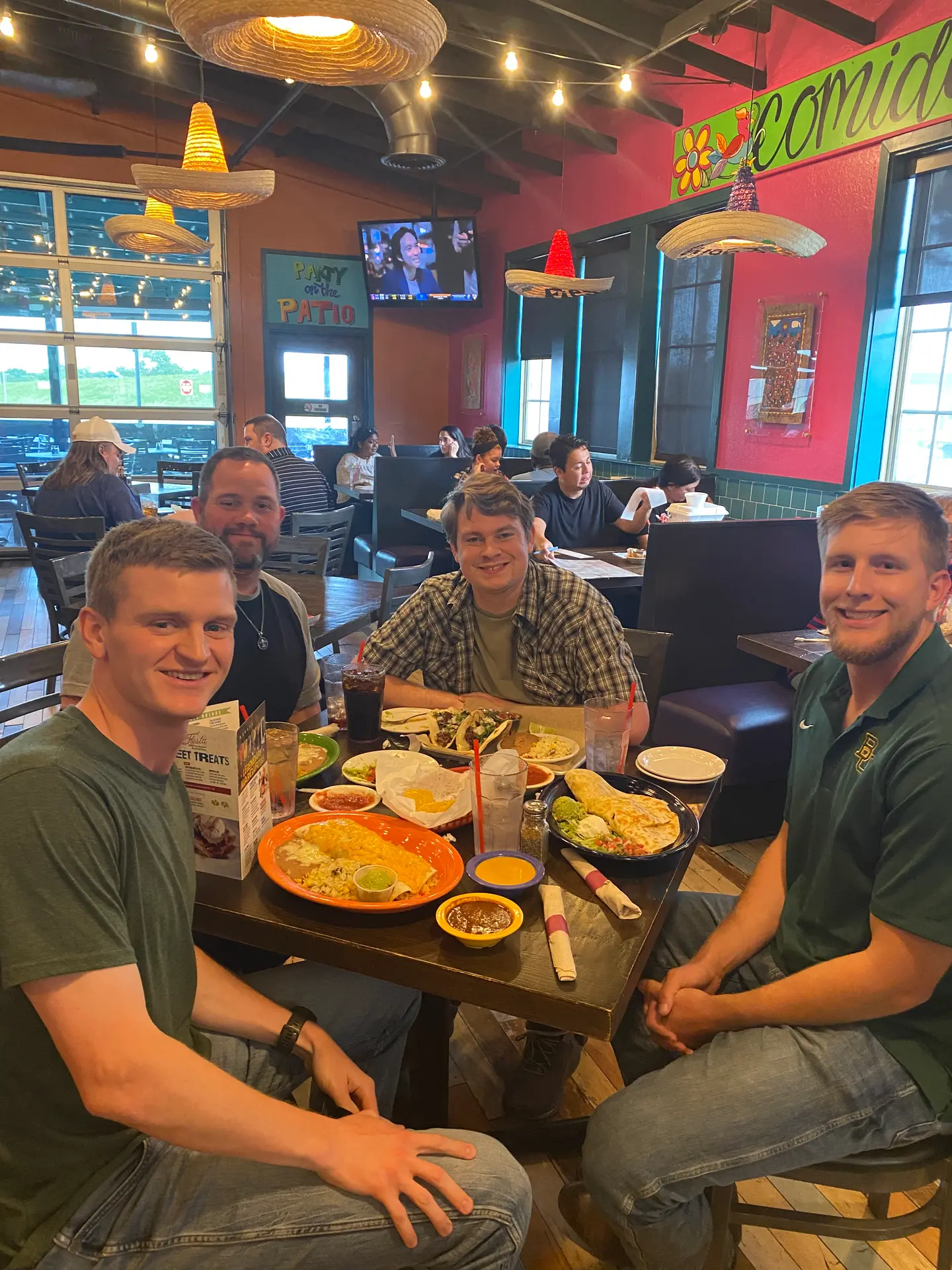 Four young men smiling at a restaurant table with Mexican food plates and drinks.