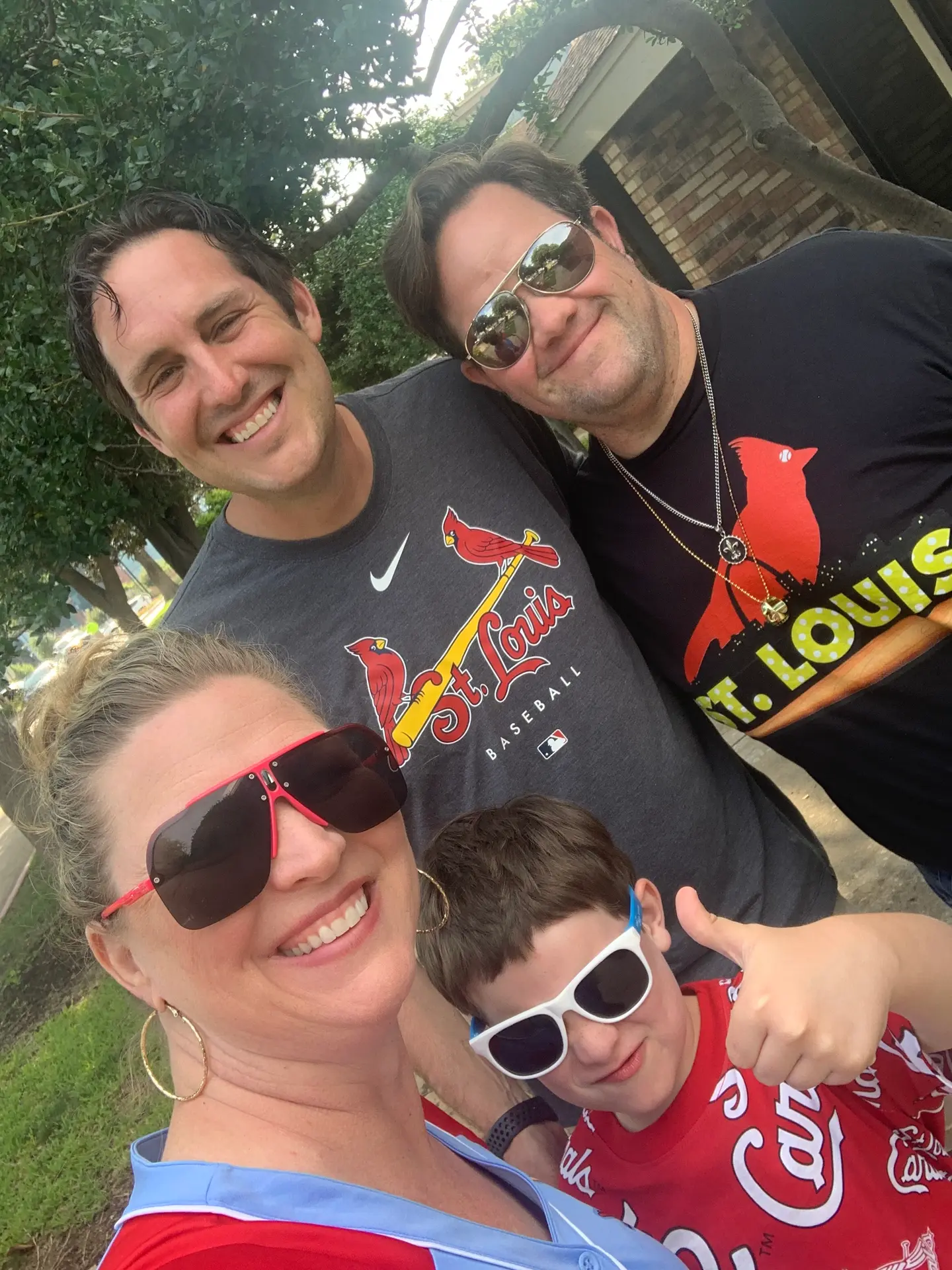 Smiling group of three adults and a boy wearing St. Louis Cardinals shirts and sunglasses outdoors.