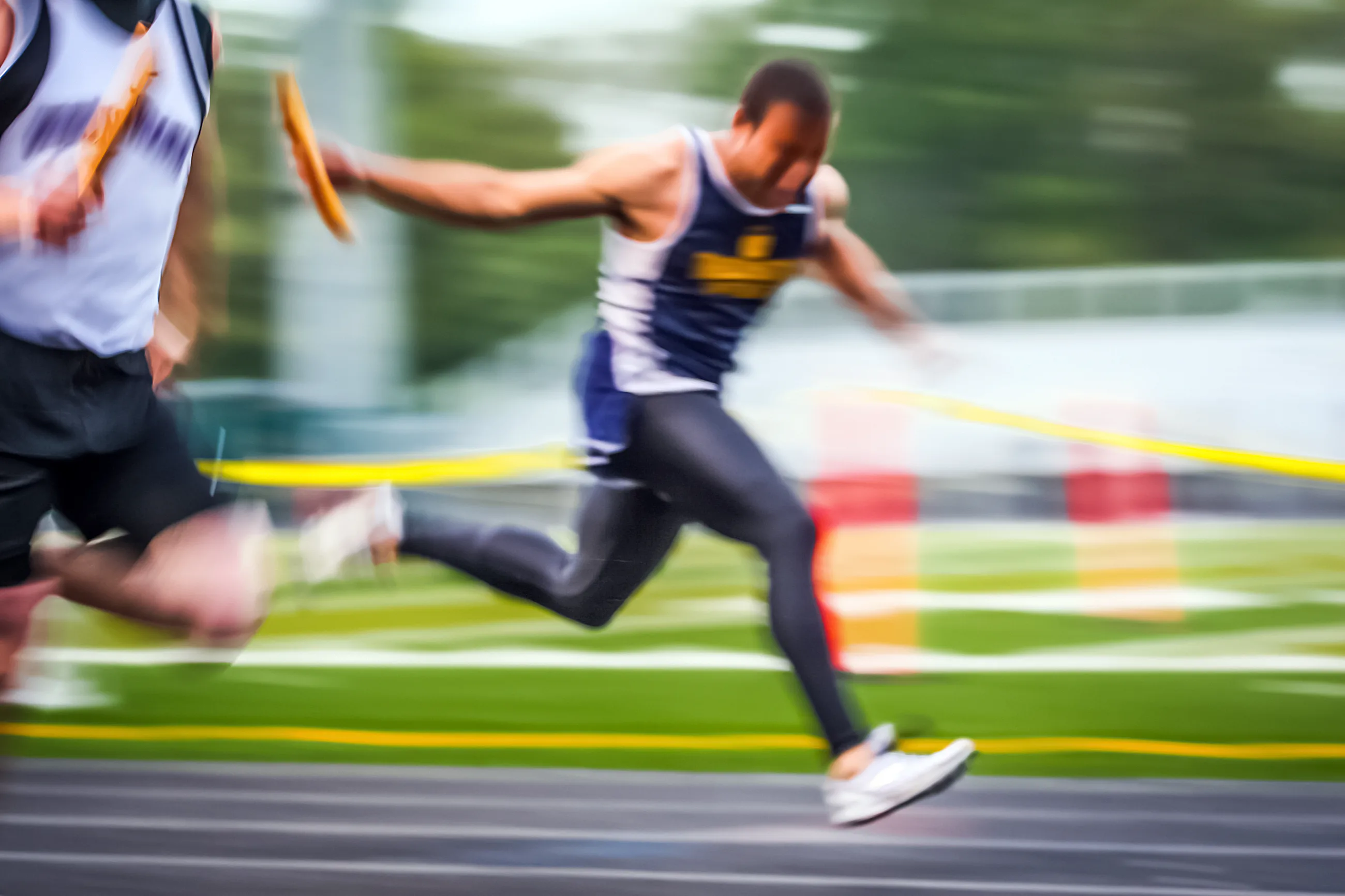 Two track athletes passing a relay baton in a race with motion blur on an outdoor track.