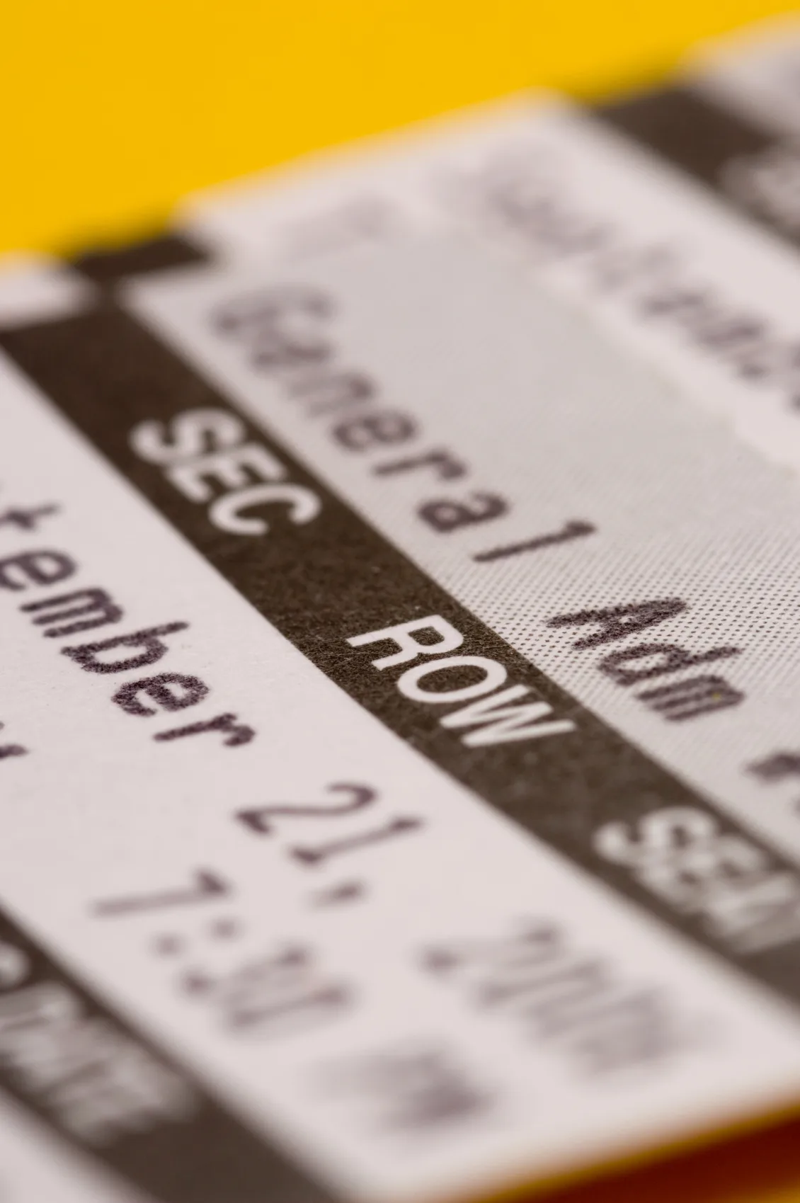 Close-up of an event ticket showing section, row, and a partial date on yellow background.