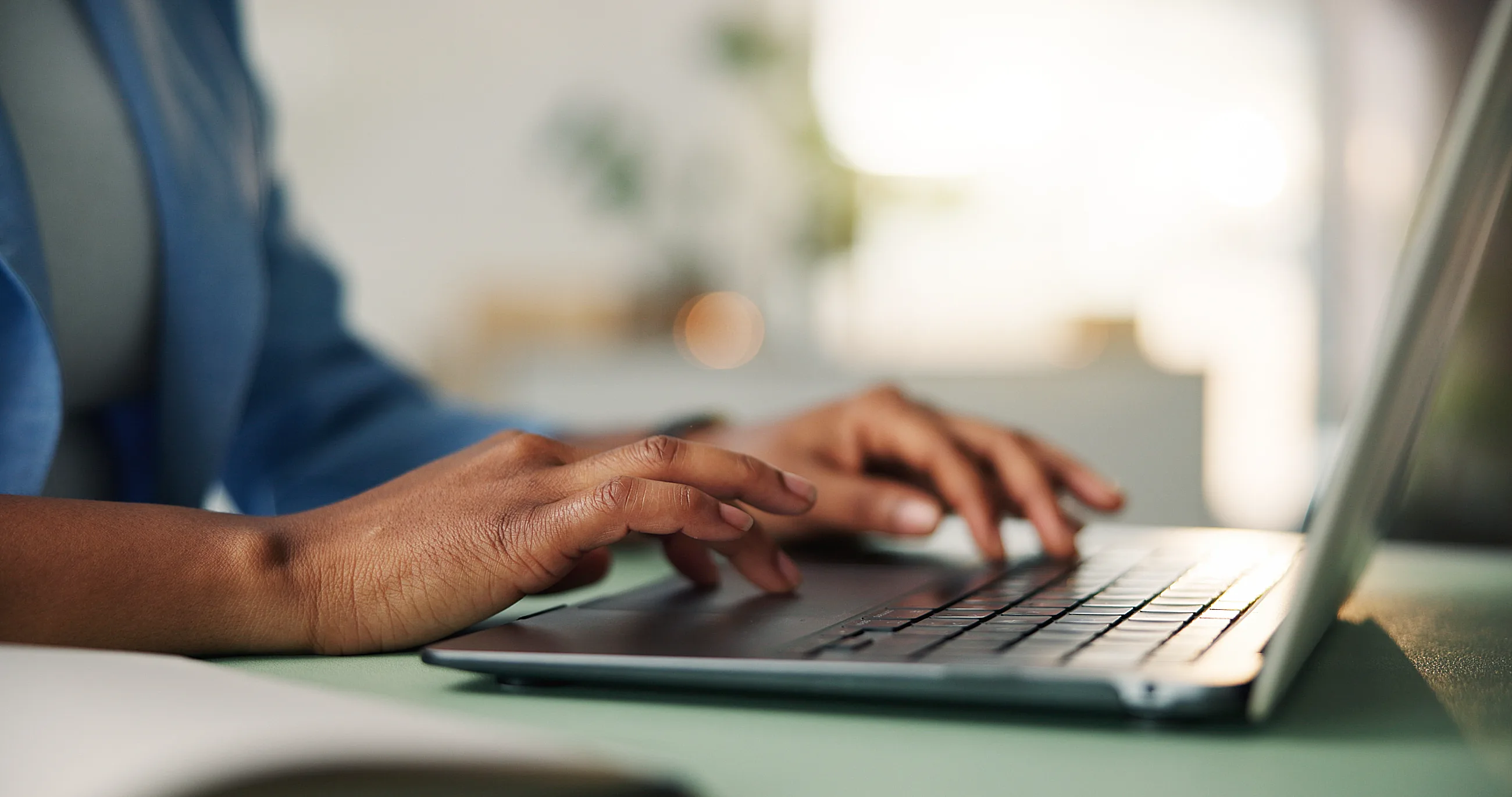Person typing on a laptop keyboard at a desk with blurred background.