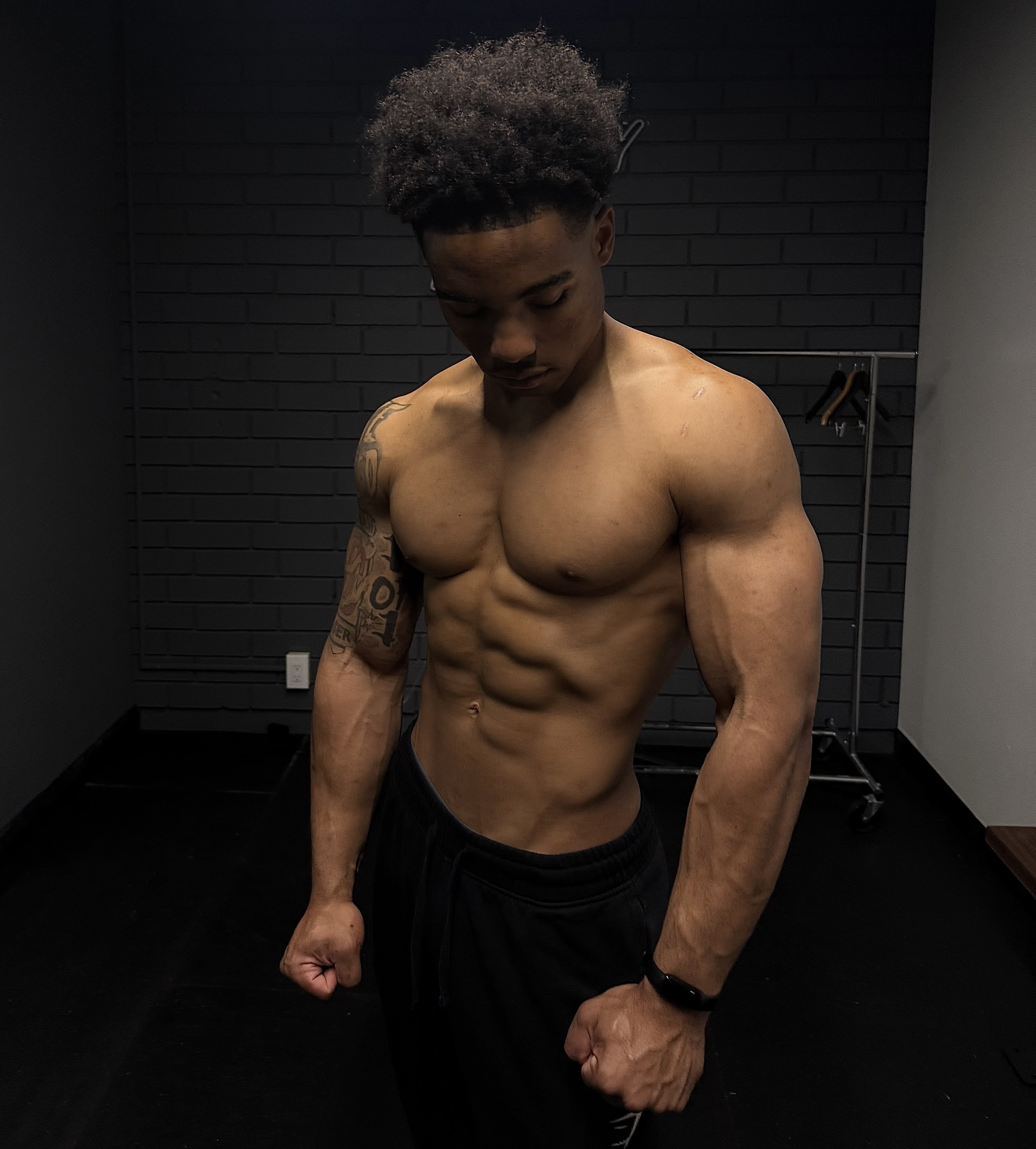 Muscular man flexing his arms and abs, looking down in a dark room.