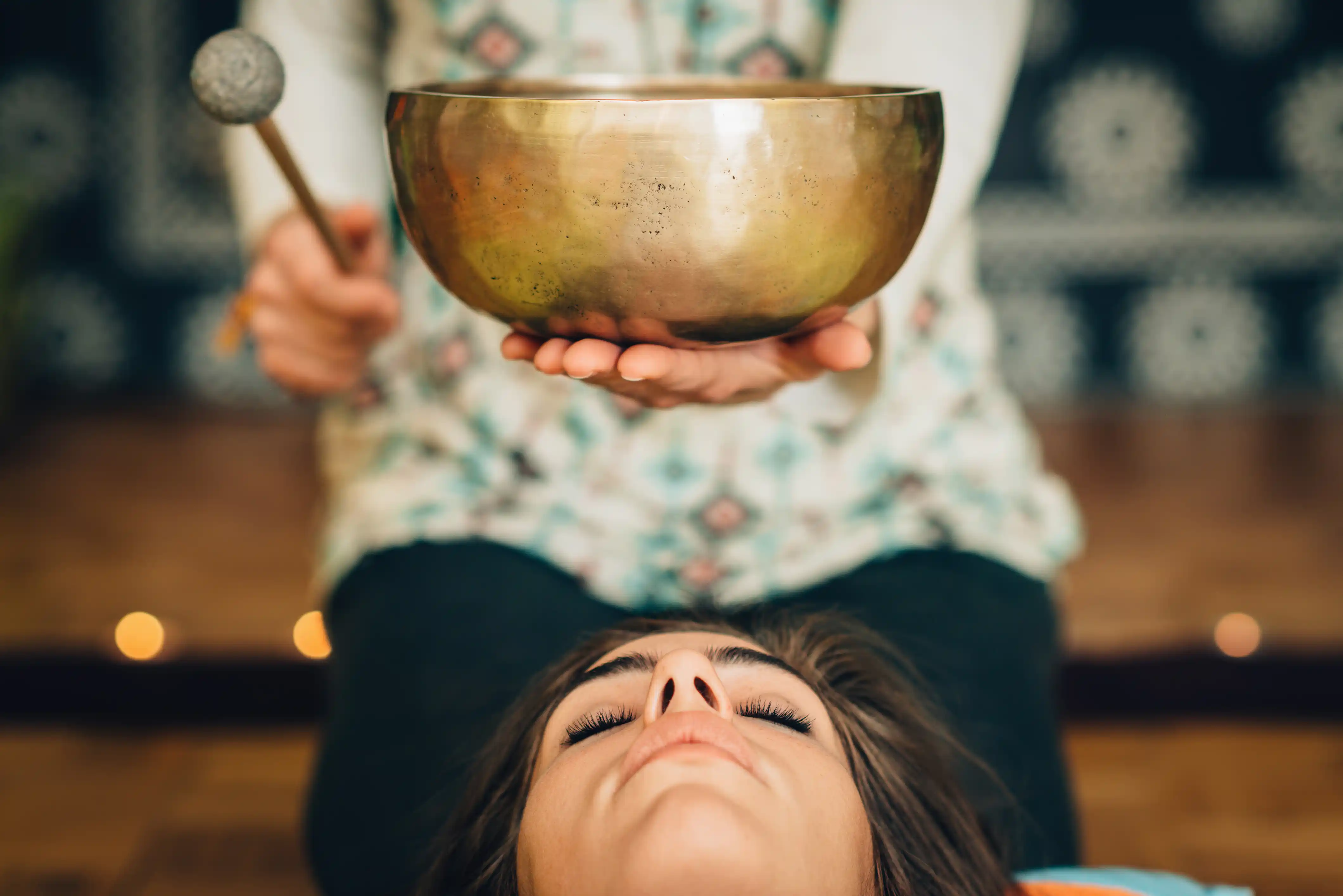 Woman lying down while a healer uses a Tibetan singing bowl for a Sound Bath