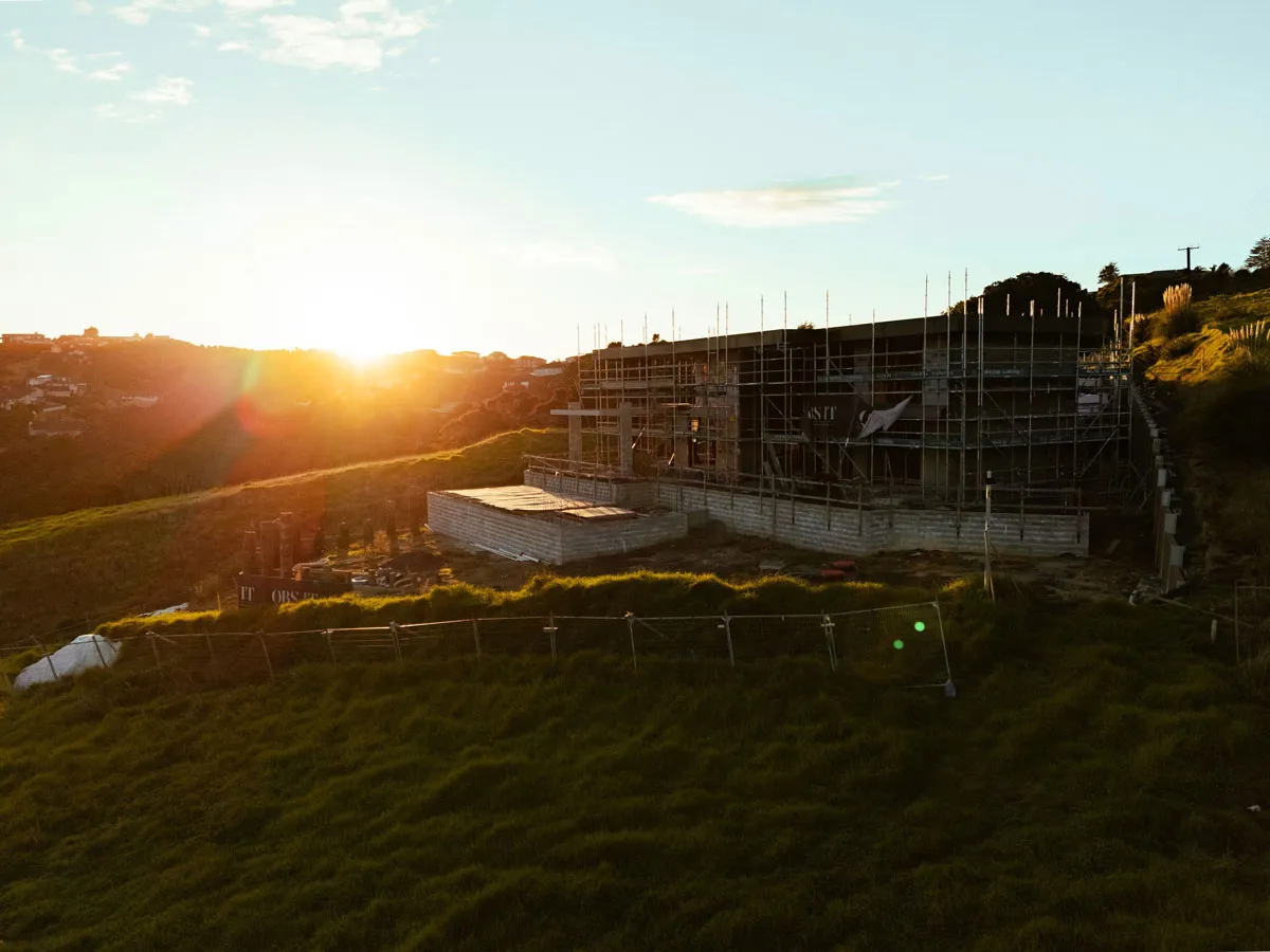 Partially built structure with scaffolding on a grassy hill during sunset.