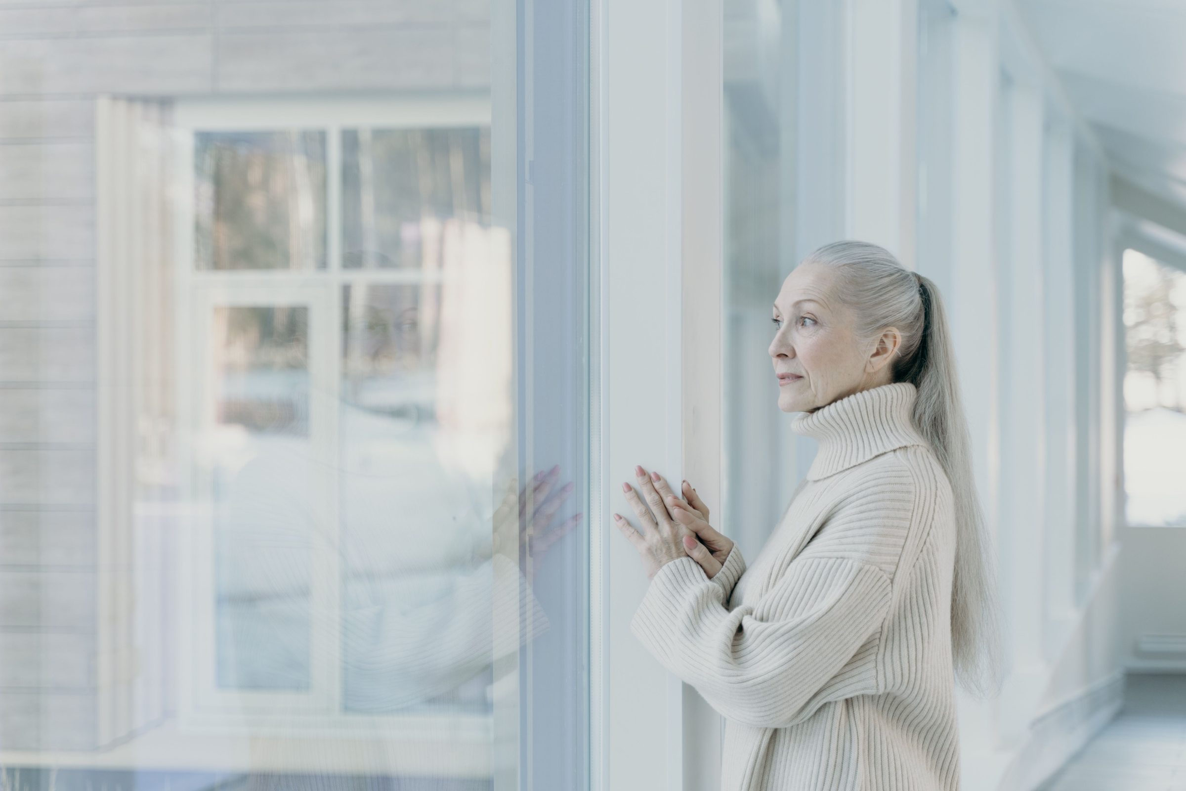 A woman looking out a large window in a bright, quiet room