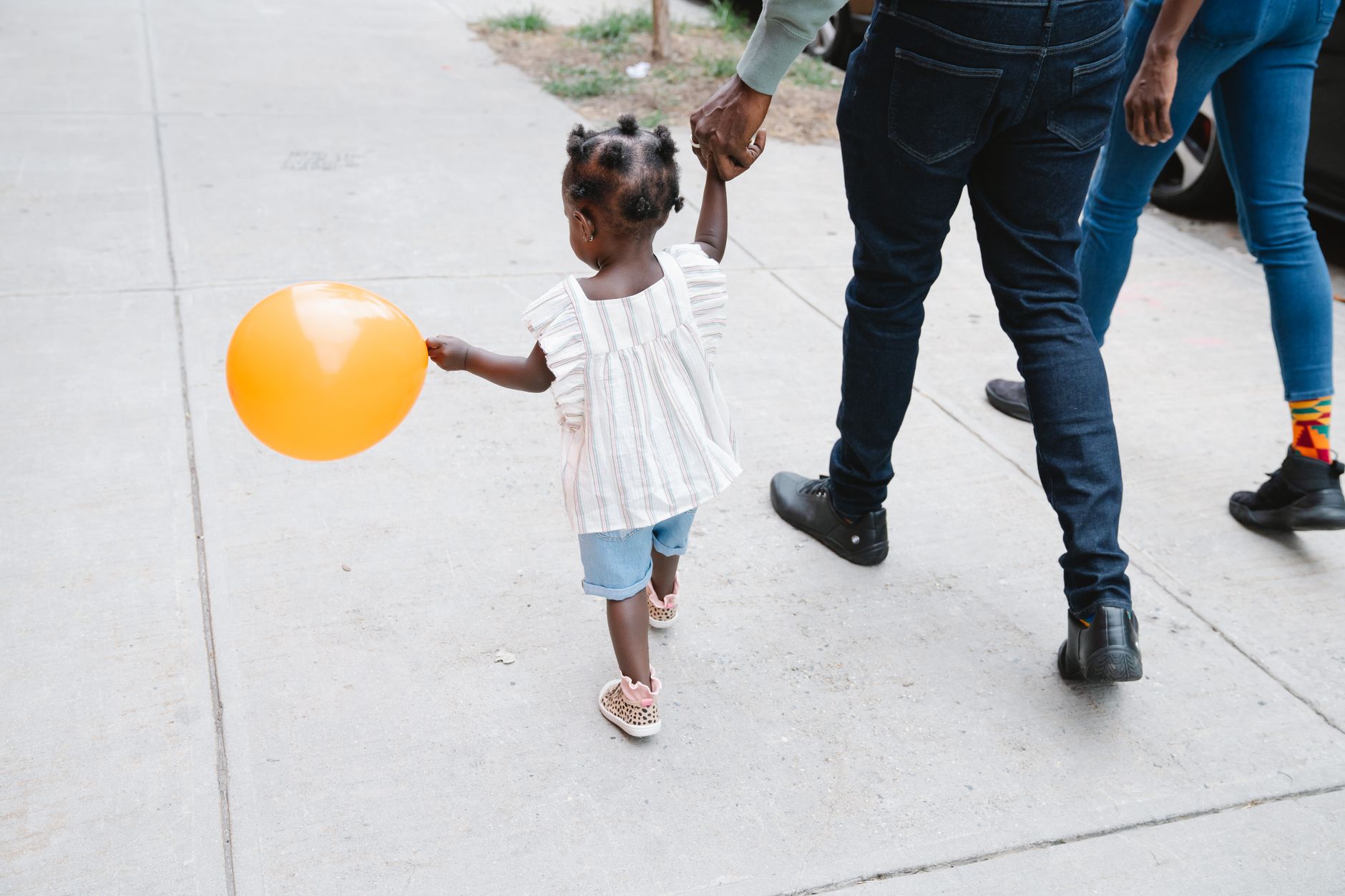 Child and parents walking on sidewalk holding hands with a colorful balloon.