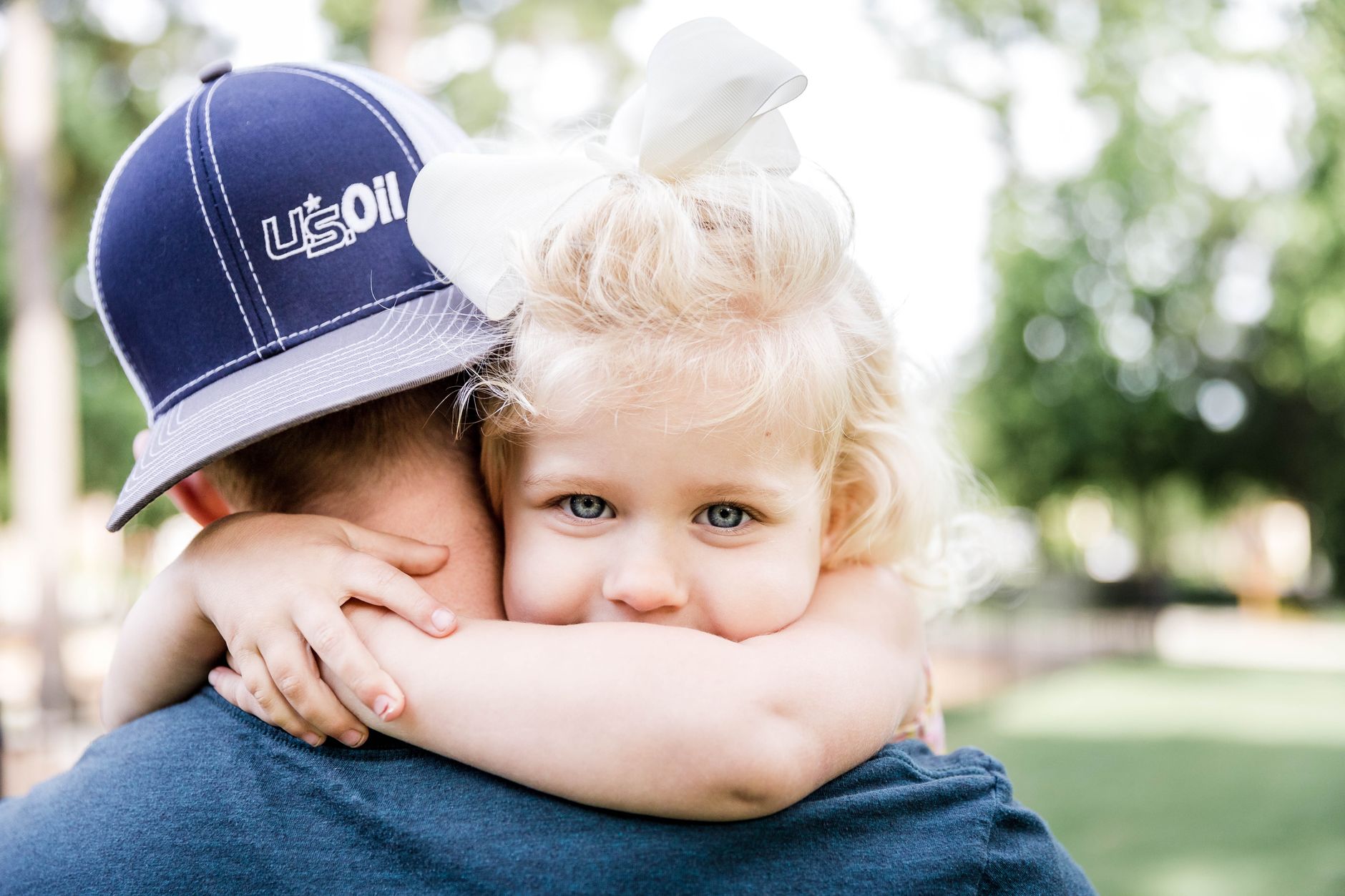 Child looking at camera while hugging dad in street in summer sunny day near trees