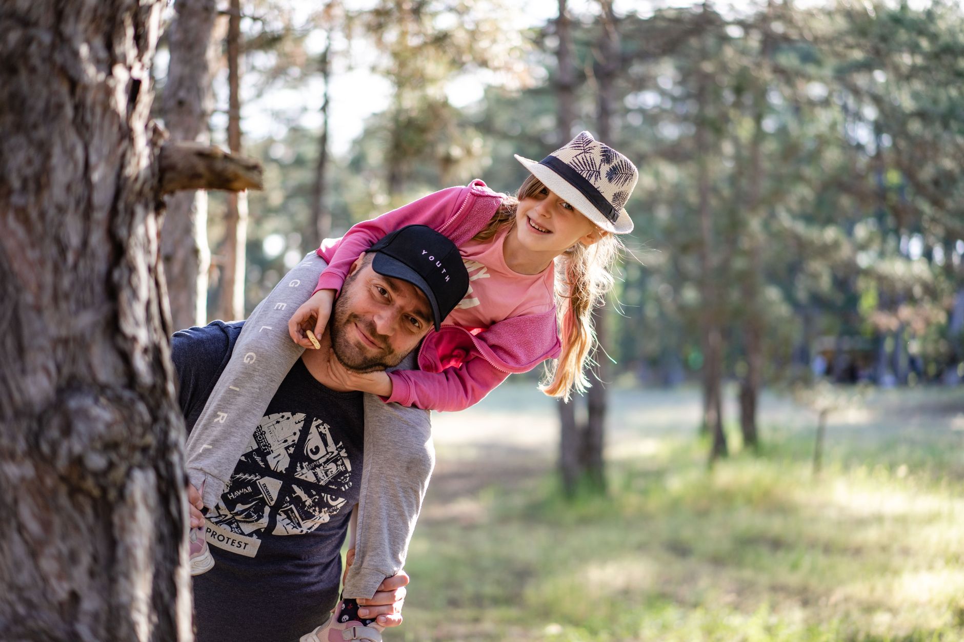 A joyful father giving his daughter a piggyback ride in a sunny forest setting.