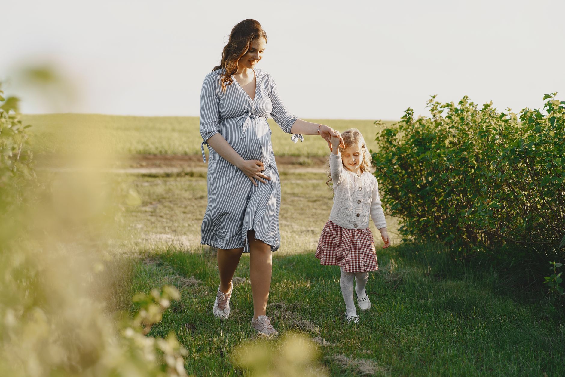 A pregnant mother enjoying a summer walk with her daughter in a green field.