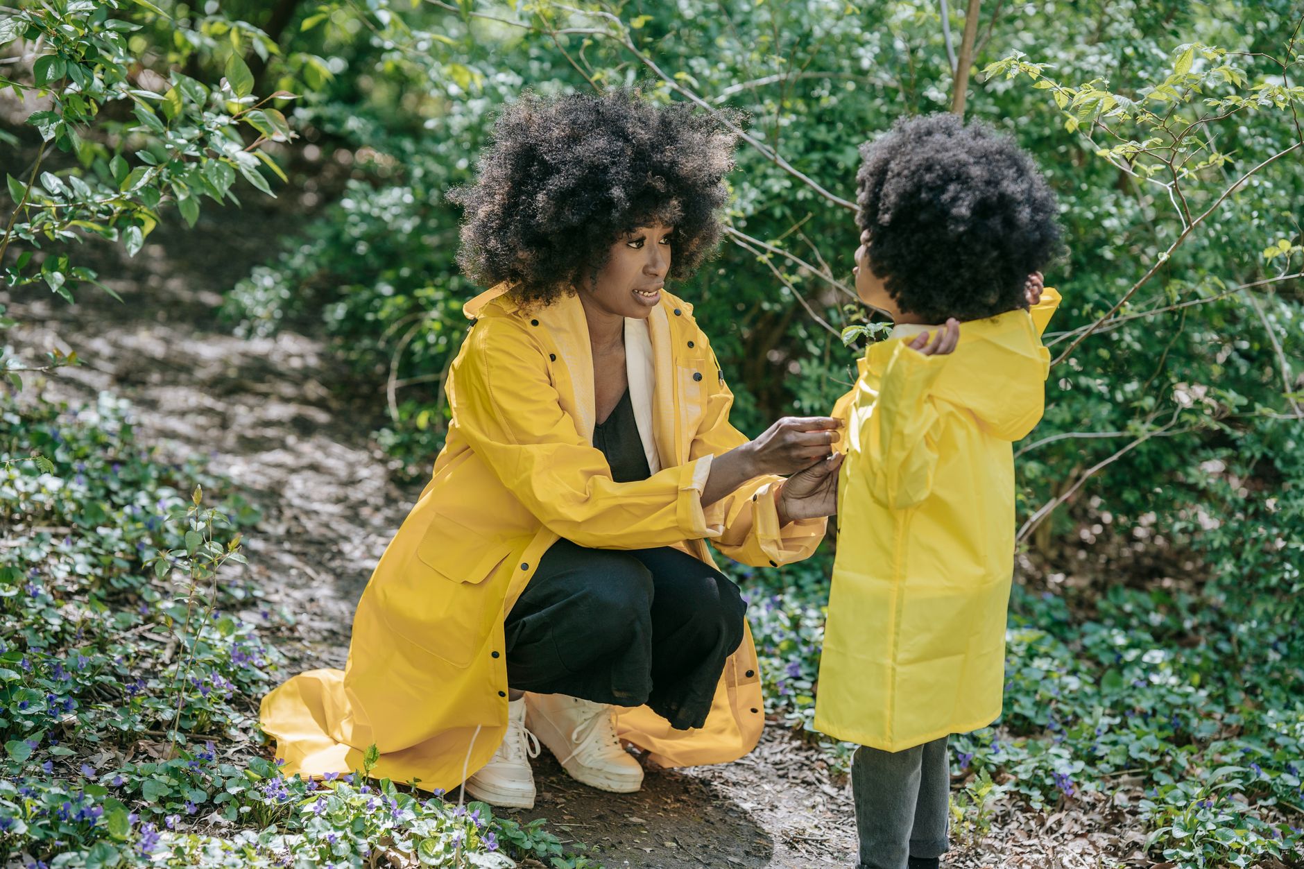 A mother and daughter bonding in nature, wearing matching yellow raincoats, showcasing togetherness.