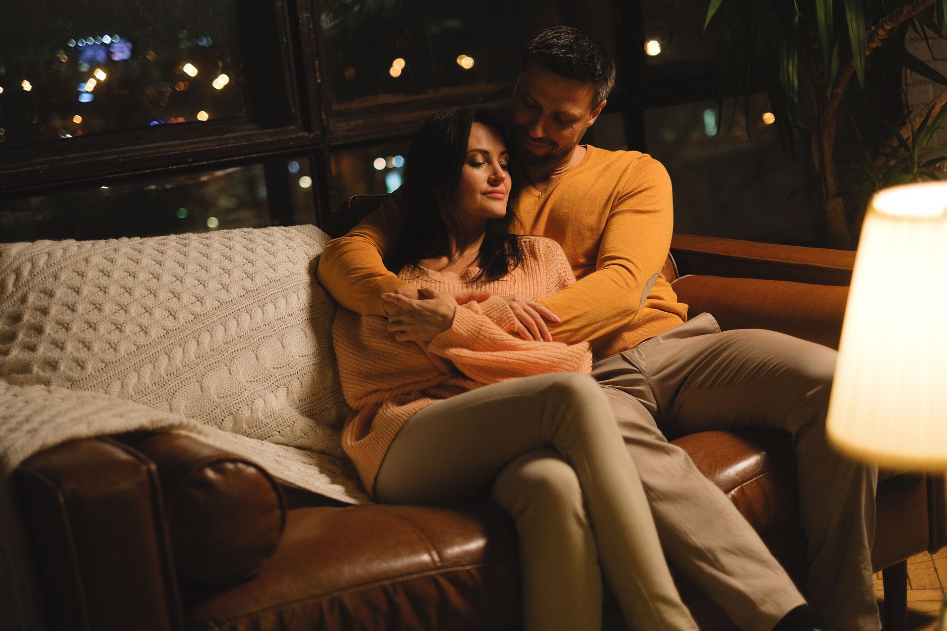 A couple embraces on a couch in a softly lit room, creating a warm and cozy atmosphere.