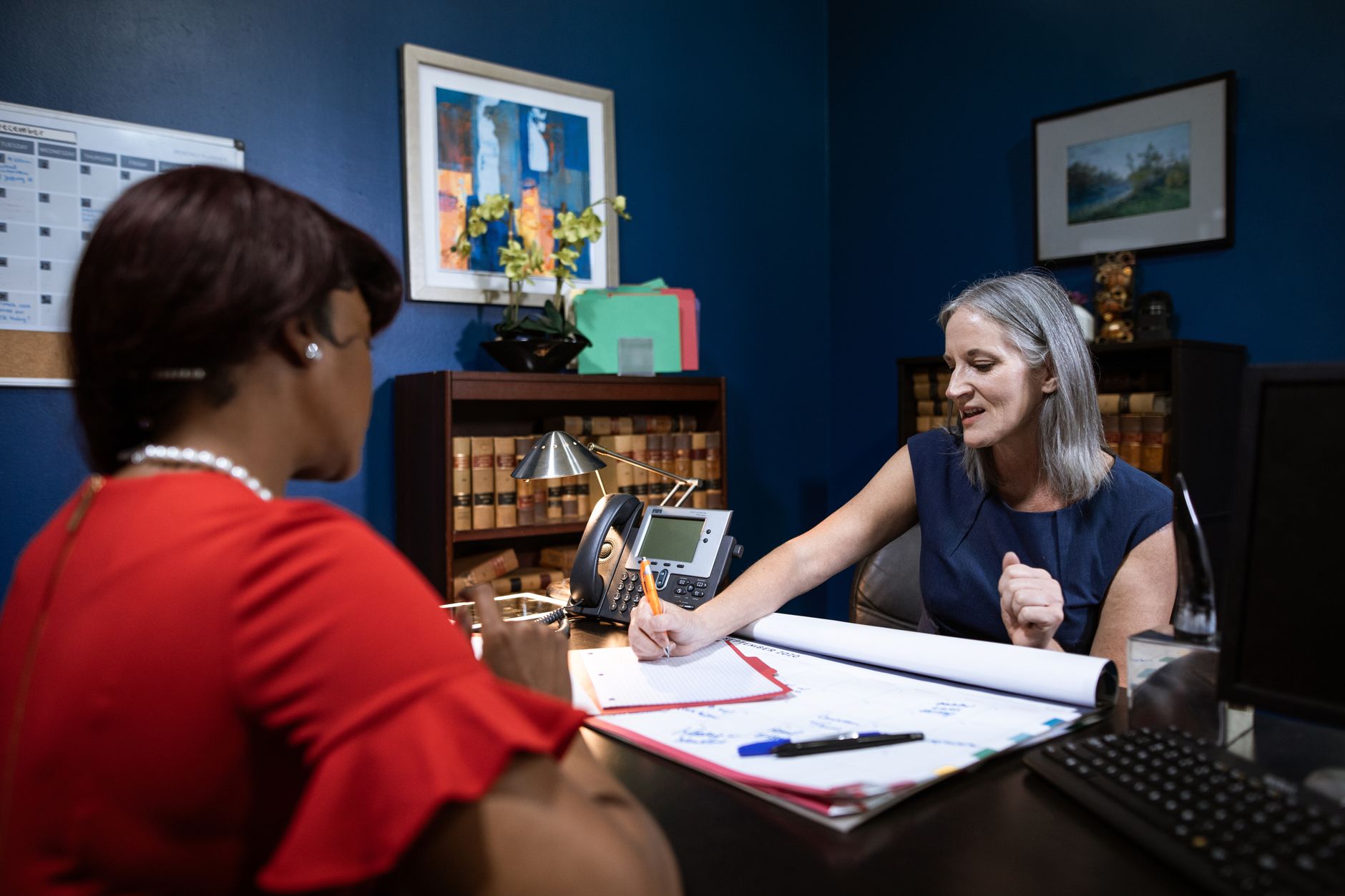 Two women engage in a work discussion in a modern office setting, captured candidly.