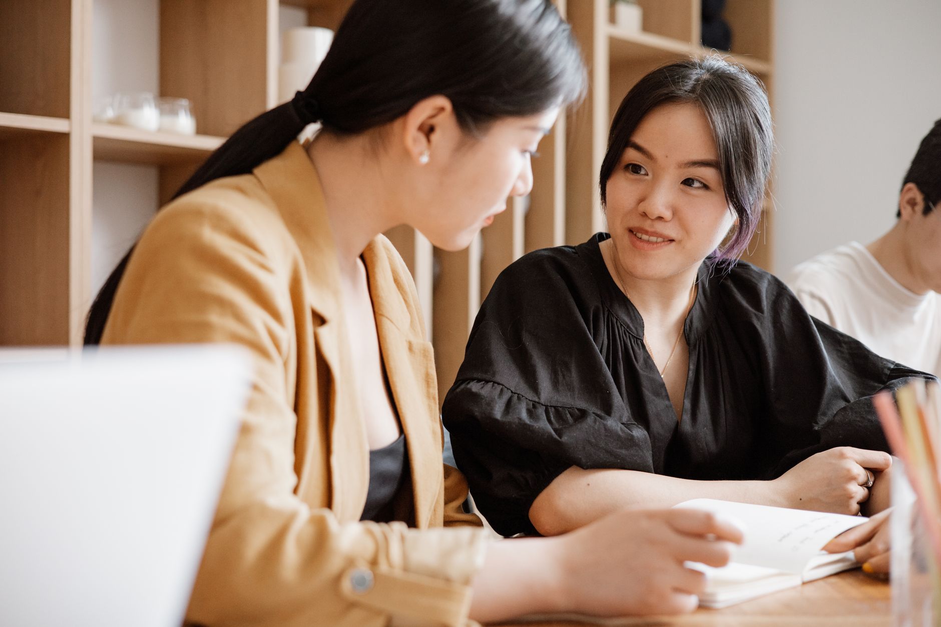 Two Asian women engaged in a professional meeting in a contemporary workspace, promoting teamwork and collaboration.